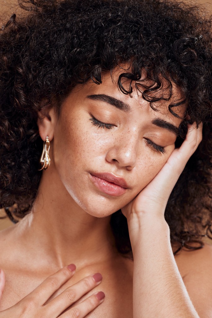 Woman with glowing skin resting her cheek on her hand