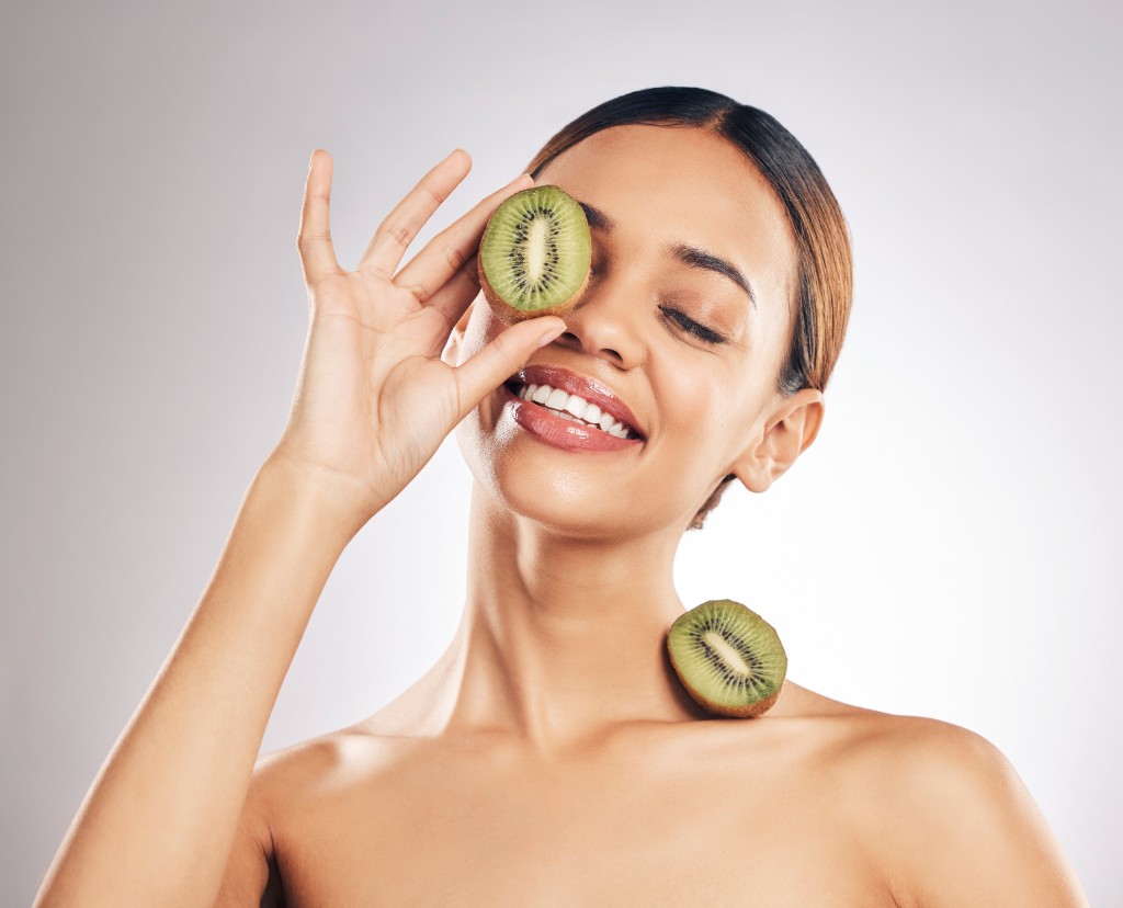 Smiling woman holding kiwi halves for a skincare moment